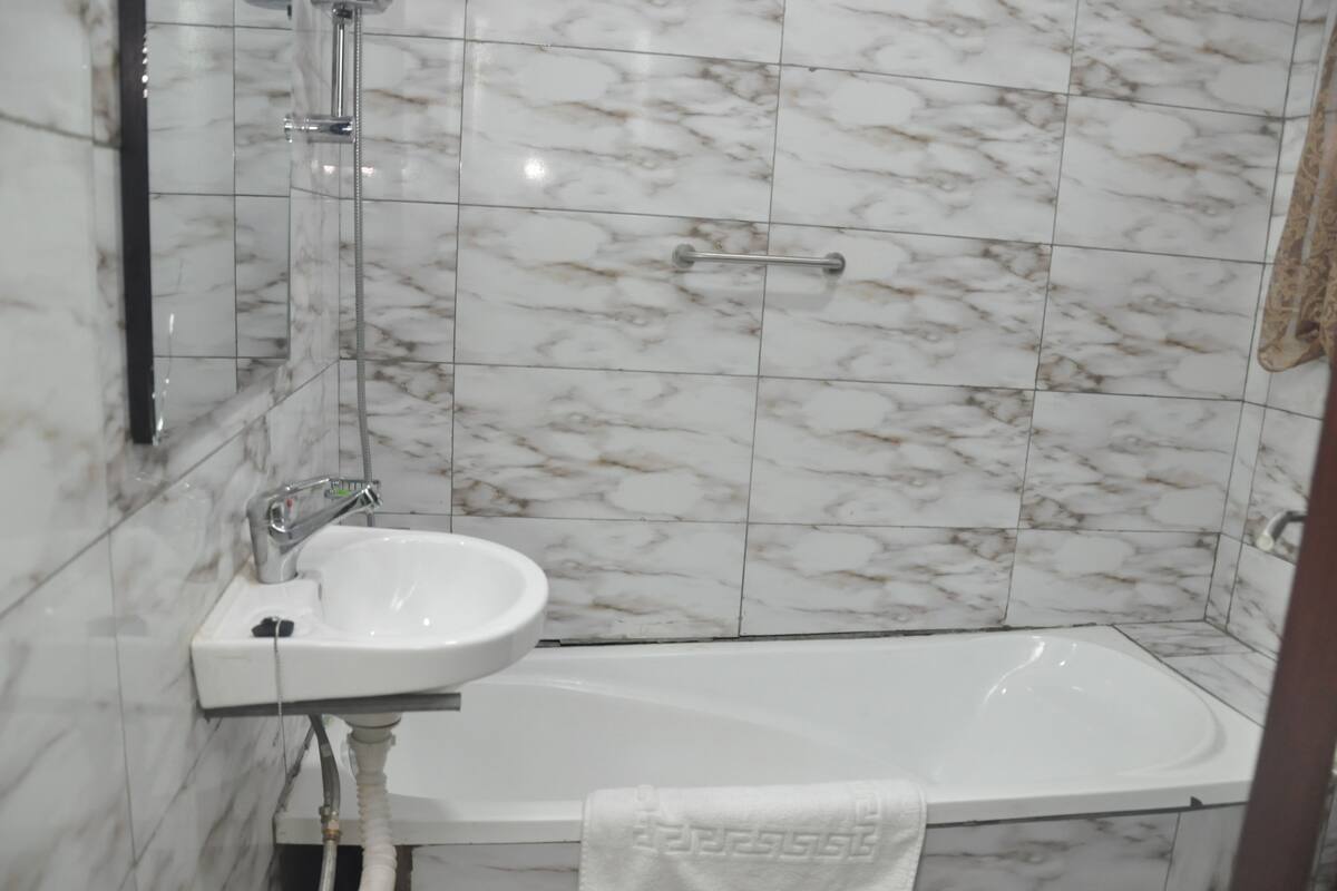 A bathroom with a white sink, a handheld showerhead, and a bathtub.