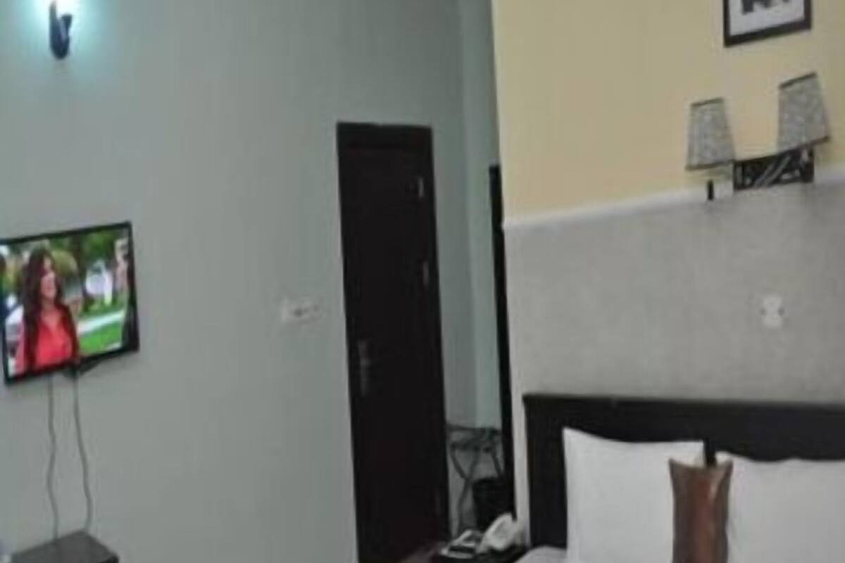 A hotel room with a bed, a TV on a stand, a desk, and a door.