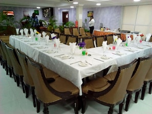 Une salle de banquet avec de longues tables dressées pour le repas, des chaises et un espace bar.
