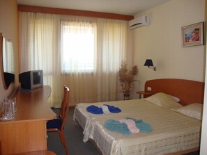 A hotel room with a bed, a desk with a computer, a chair, a lamp, and a window with curtains. - Hotel Fiesta (Varna)
