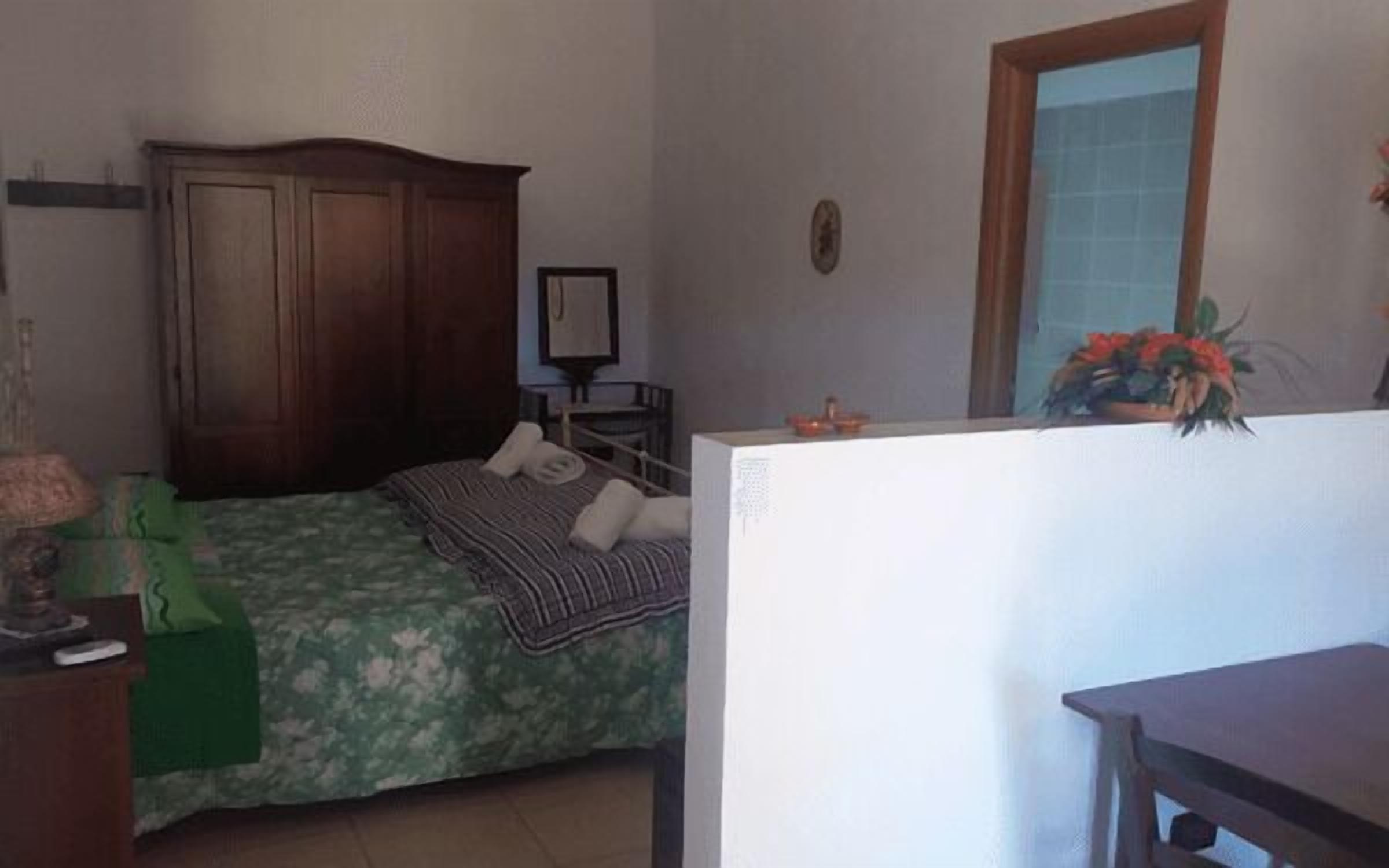 A bedroom with a bed, a wooden wardrobe, a desk, and a mirror.