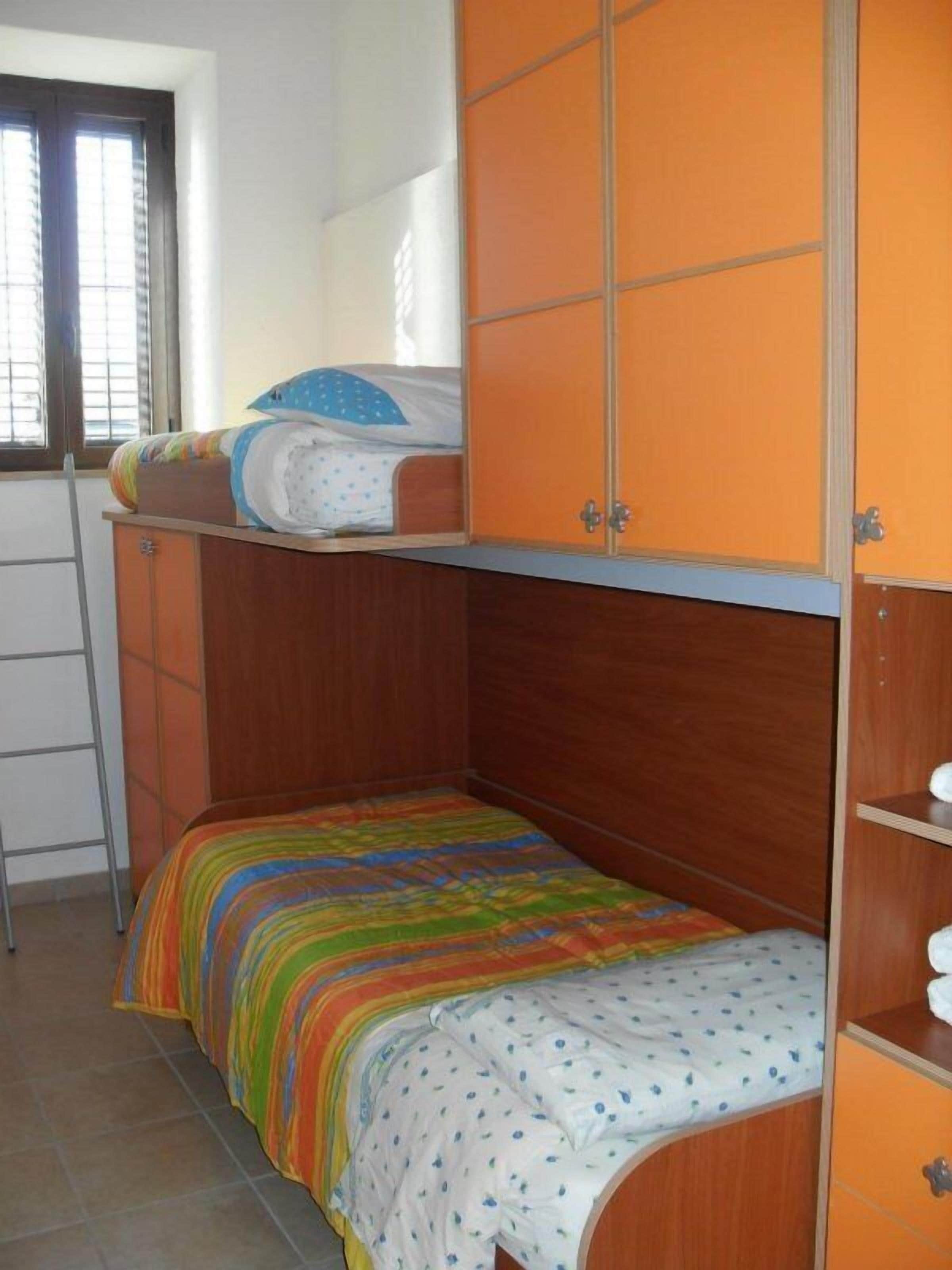 A small, single-bed room with a wooden bunk bed and a colorful striped bedspread.
