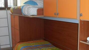A small, single-bed room with a wooden bunk bed and a colorful striped bedspread.