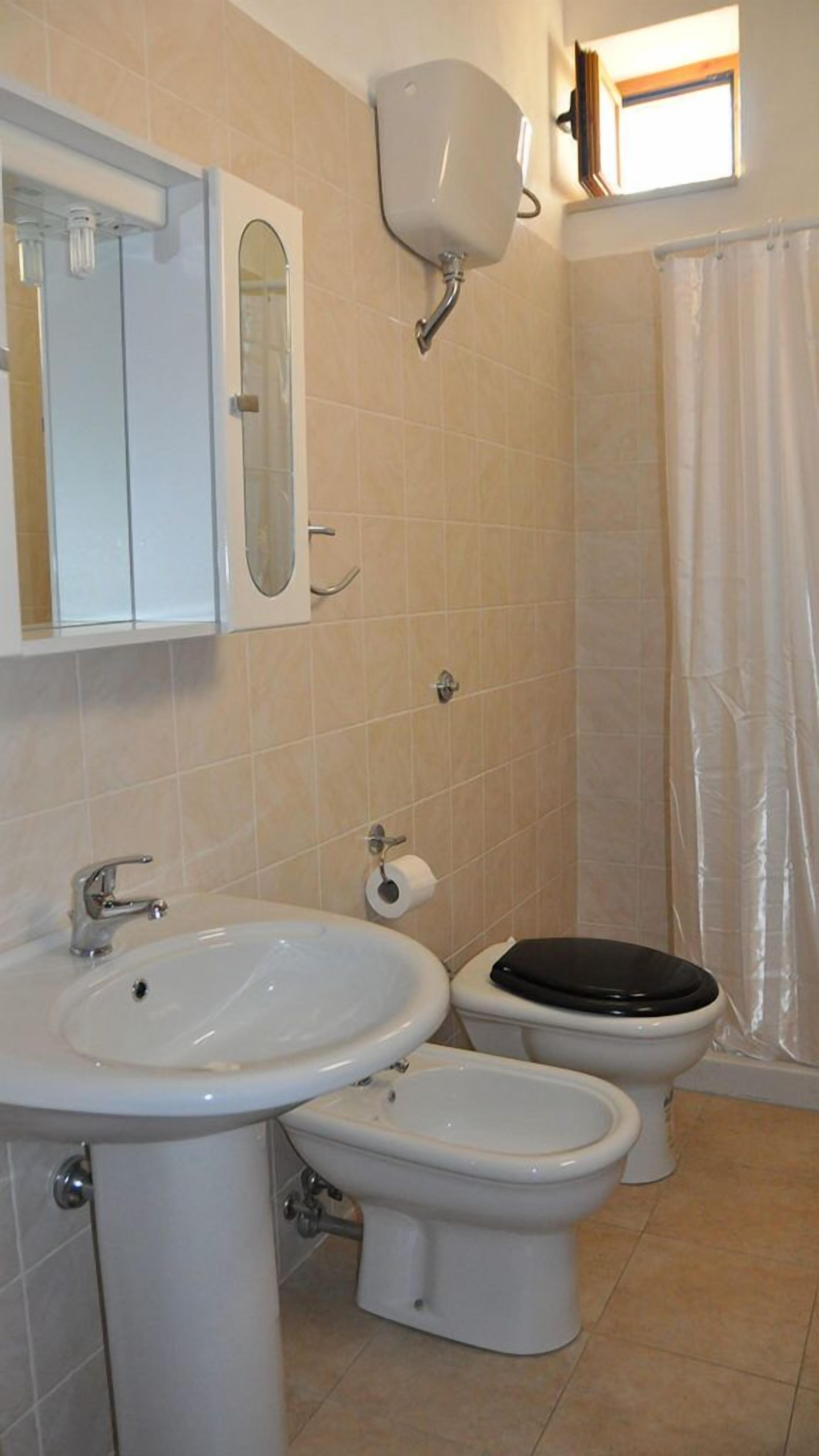 Ein Badezimmer mit Waschbecken, zwei Toiletten, einem Spiegel und einer Duschvorhang.
