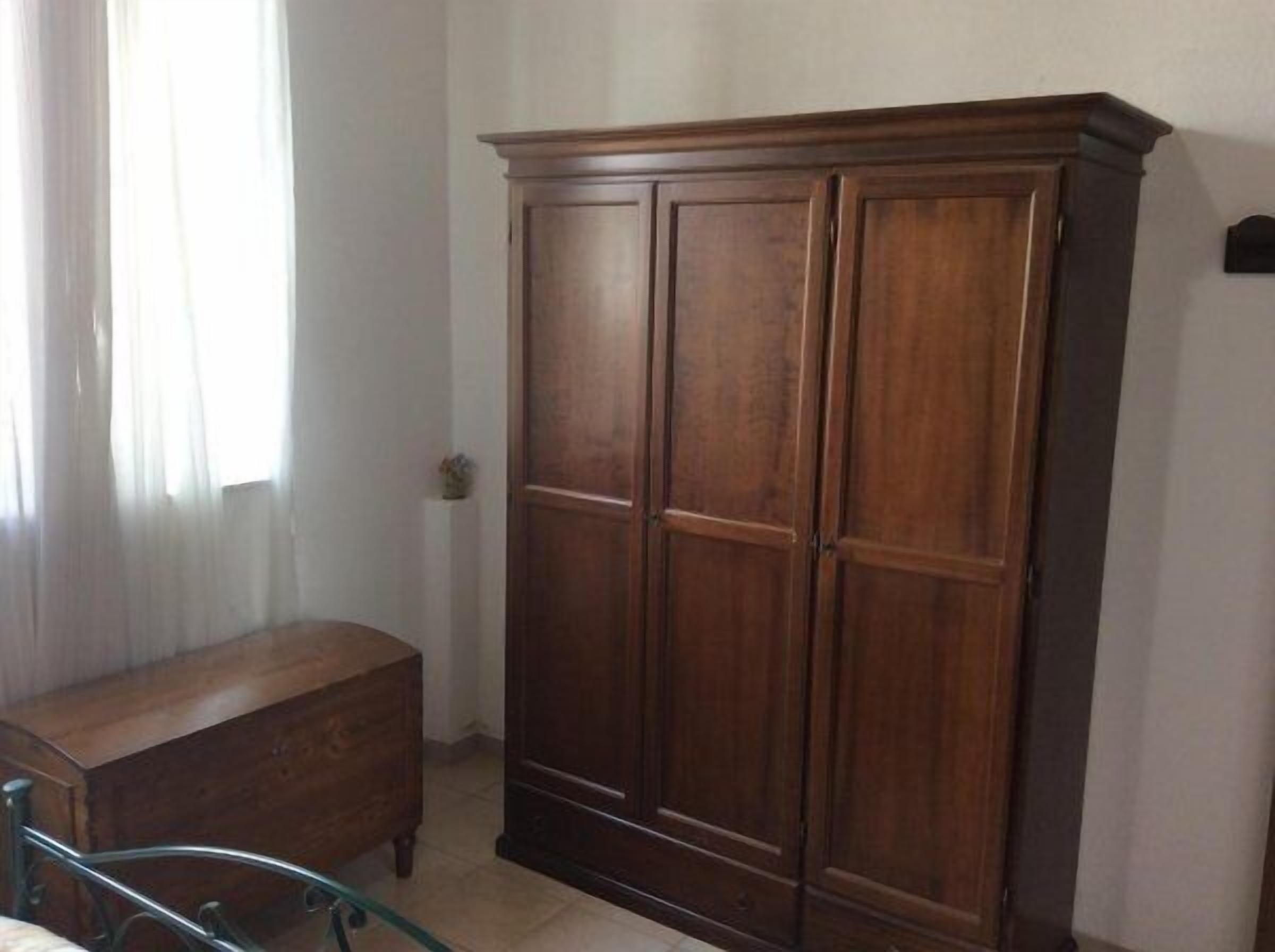 Una habitación con un armario de madera, una cómoda pequeña de madera y una silla con estructura de metal.