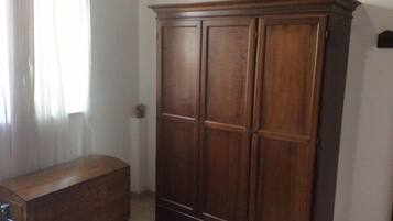 Una habitación con un armario de madera, una cómoda pequeña de madera y una silla con estructura de metal.