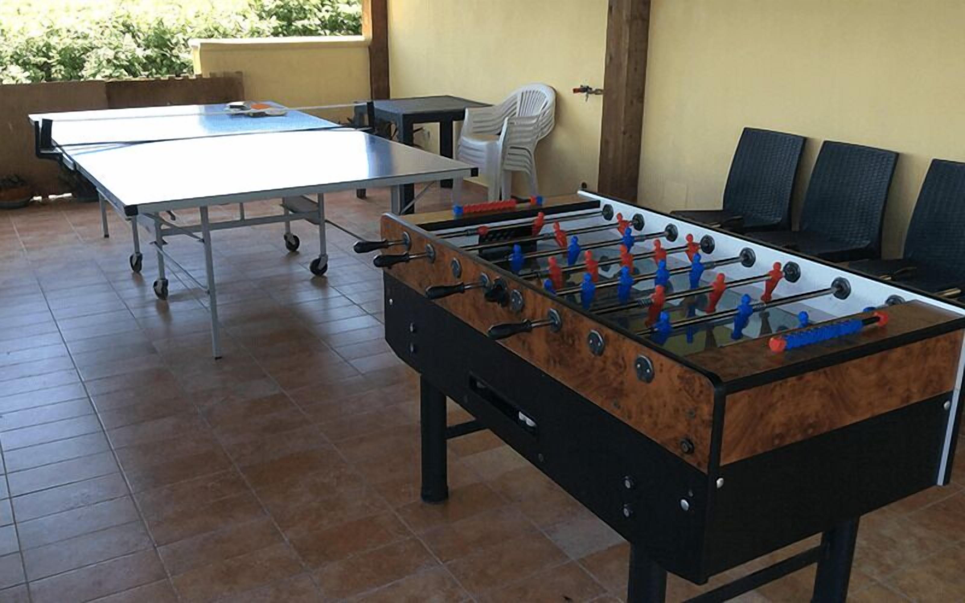 A foosball table in a room with a tiled floor, a white plastic chair, and a table with a blue tablecloth.