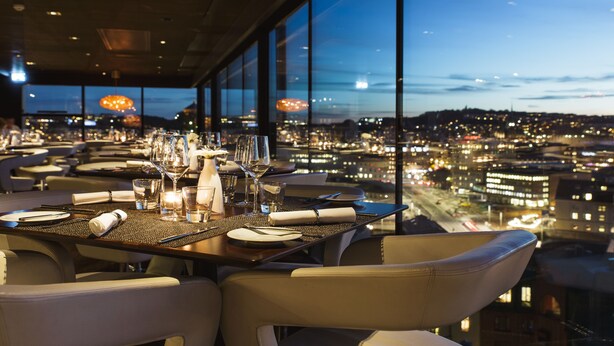 Comedor con una mesa lista para dos personas, amplias ventanas con vista a la ciudad al atardecer.
