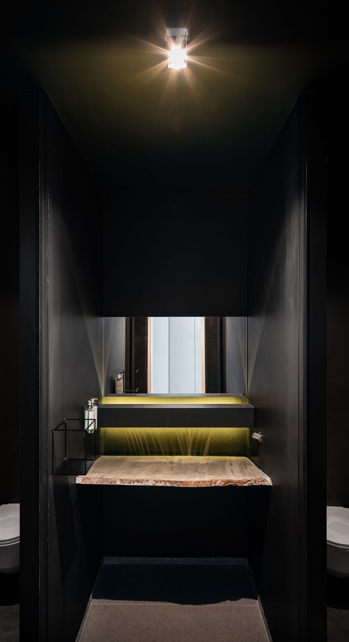 A narrow, dimly lit bathroom with a bench, a mirror, and a window.