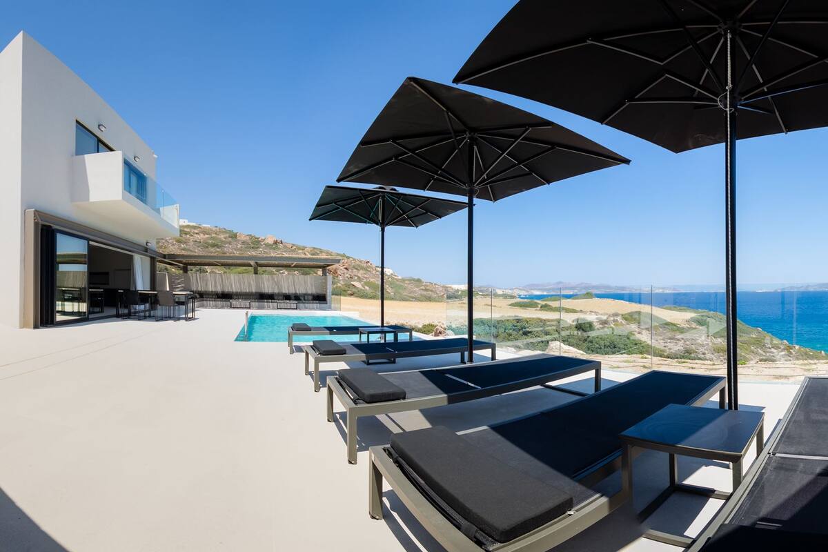 A modern outdoor pool area with lounge chairs and umbrellas, overlooking a scenic coastline.