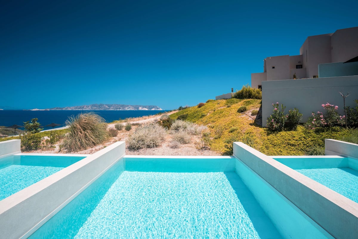 A modern pool area with clear blue water, surrounded by greenery and overlooking a coastal landscape.