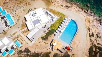 An aerial view of a resort with multiple swimming pools, a large central pool, and a beach area.