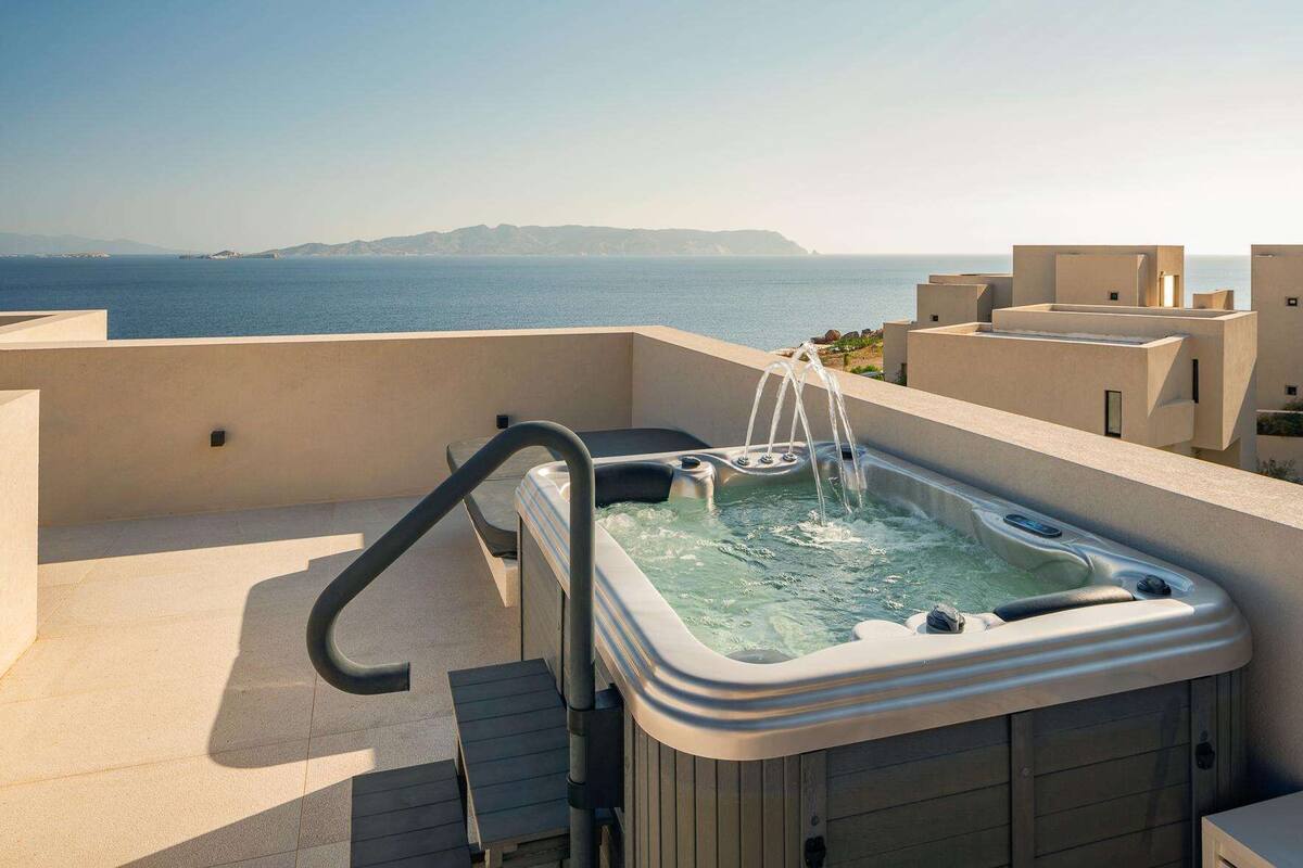 A hot tub on a rooftop with a view of the sea and distant hills.