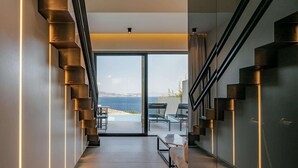 A modern interior with a staircase leading to a balcony overlooking the sea.