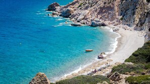 A coastal beach with clear turquoise waters, rocky cliffs, and a row of sun umbrellas.