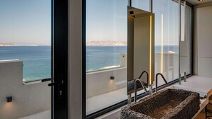 A modern bathroom with a large window offering a sea view, a stone sink, and a minimalist design.