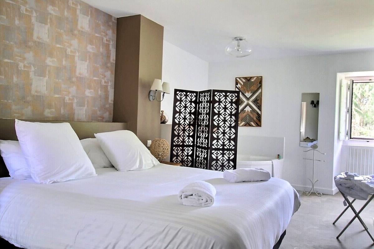 Une chambre d’hôtel avec un grand lit, un paravent décoratif, une petite table et une fenêtre donnant sur un beau paysage.