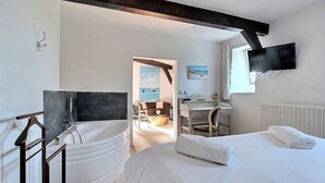 Une chambre d’hôtel avec un grand lit, un bureau avec une chaise, une salle de bain avec une baignoire et un téléviseur fixé au mur.