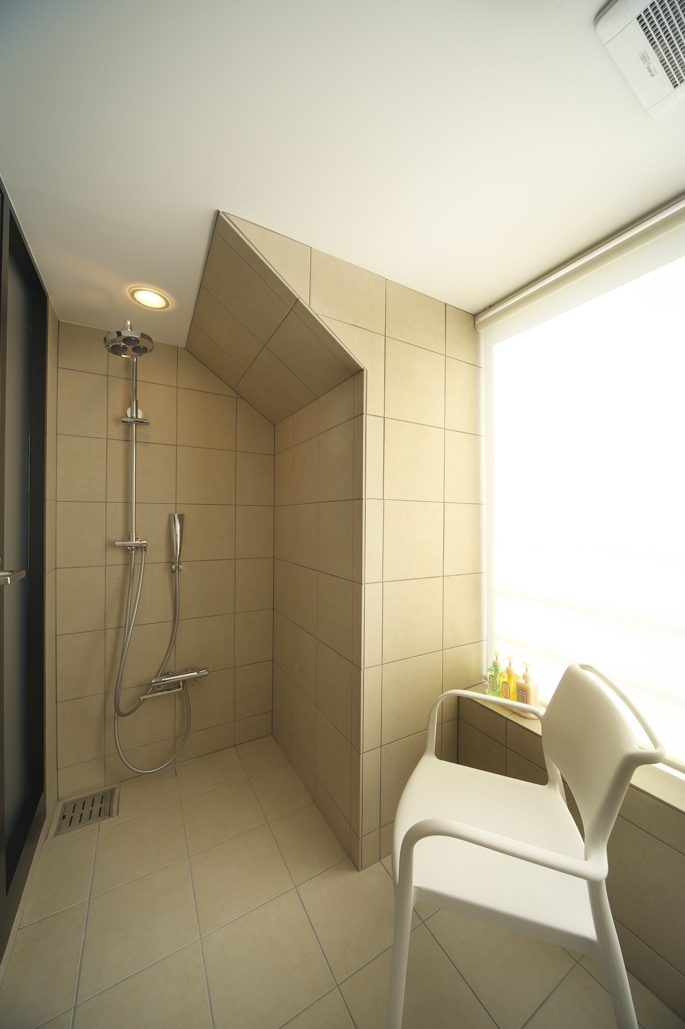 A shower area with a white chair, a showerhead, and a window.