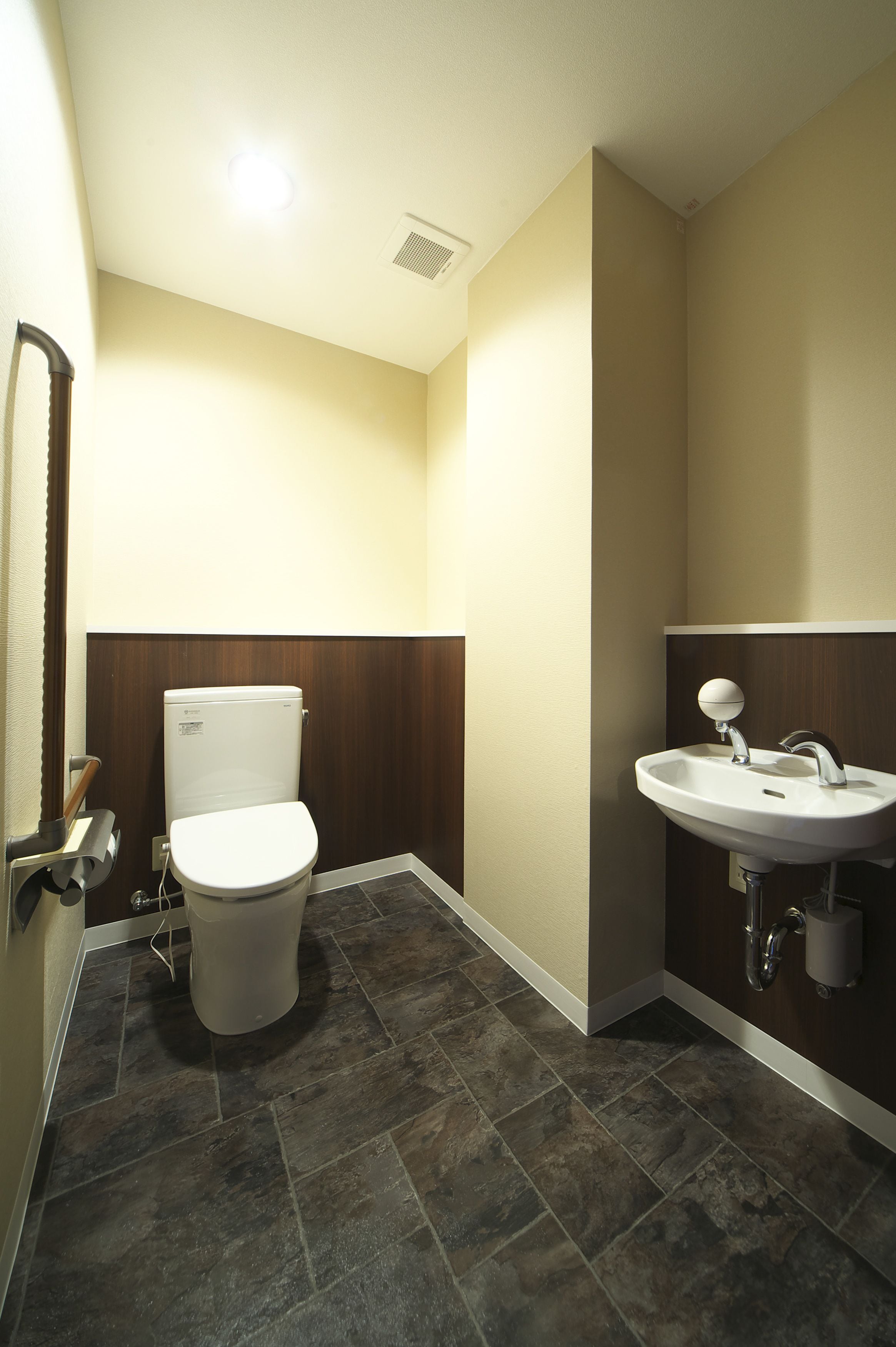 Une salle de bain avec des toilettes, un lavabo et un sol carrelé de couleur sombre.