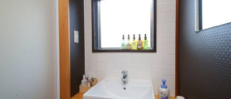Een badkamer met een witte wastafel, een raam erboven en toiletartikelen op het aanrecht.