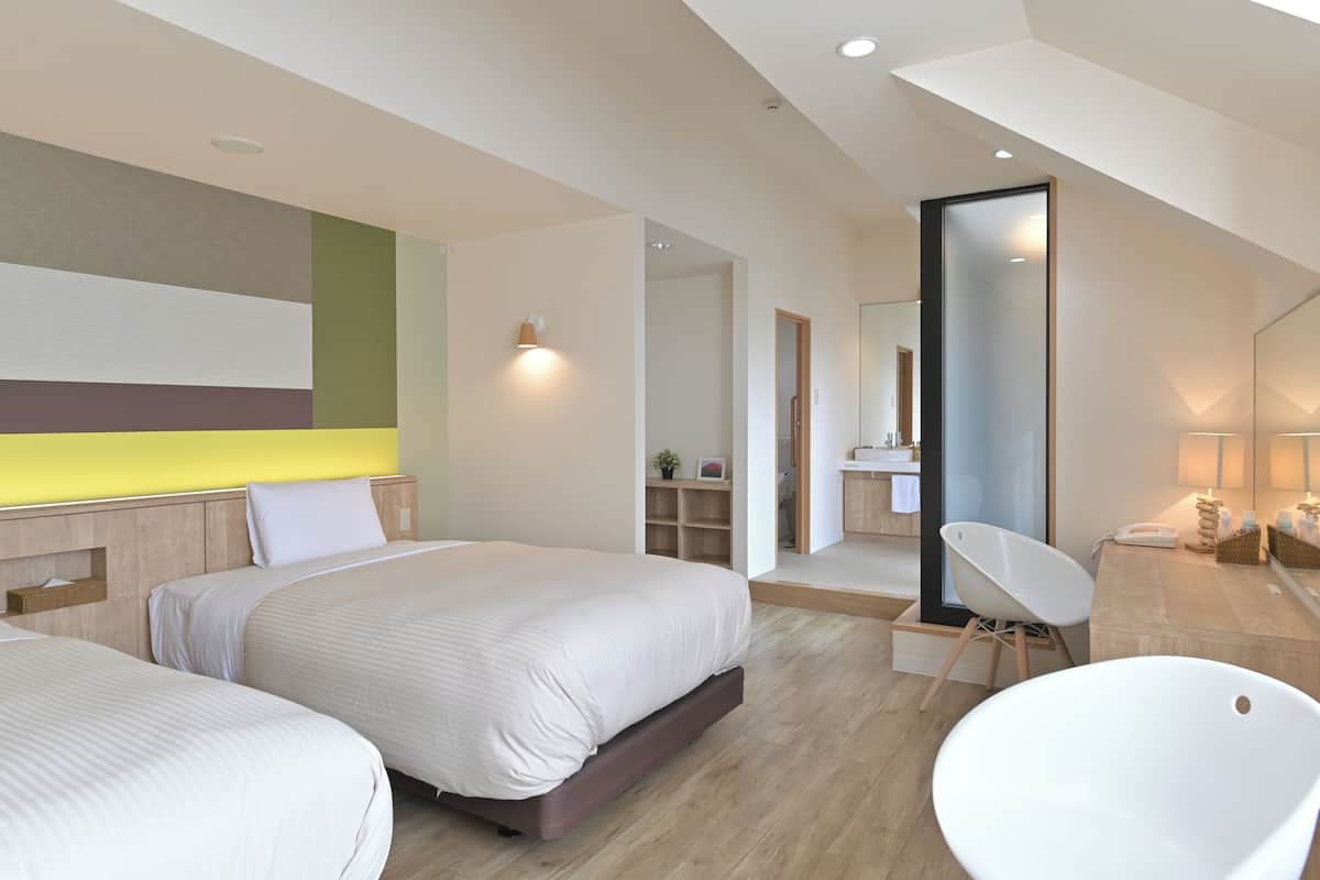 A modern bedroom with two beds, a large mirror, a bathtub, and a small bathroom.