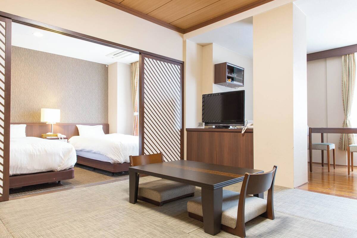 A hotel room with two beds, a TV, a desk, and a chair.