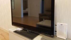 A flat-screen TV on a stand with a remote control and a white device beside it. - TnJ Home (Kota Kinabalu)