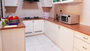 A kitchen with white cabinets, a stainless steel sink, a gas stove, a microwave, and a red fruit basket. - TnJ Home (Kota Kinabalu)