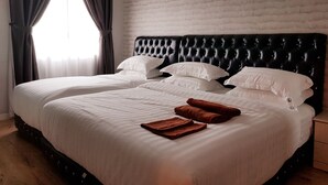 A double bed with white linens and two brown towels, a black tufted headboard, and a brick-patterned wall. - TnJ Home (Kota Kinabalu)