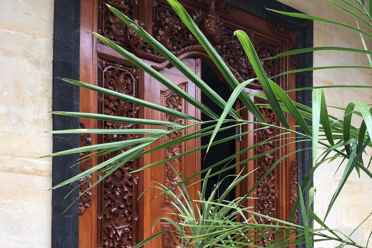 A wooden table with a potted plant, surrounded by chairs, in front of a carved wooden door.