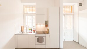 Une cuisine moderne avec des meubles blancs, un four encastré et une fenêtre équipée de stores.