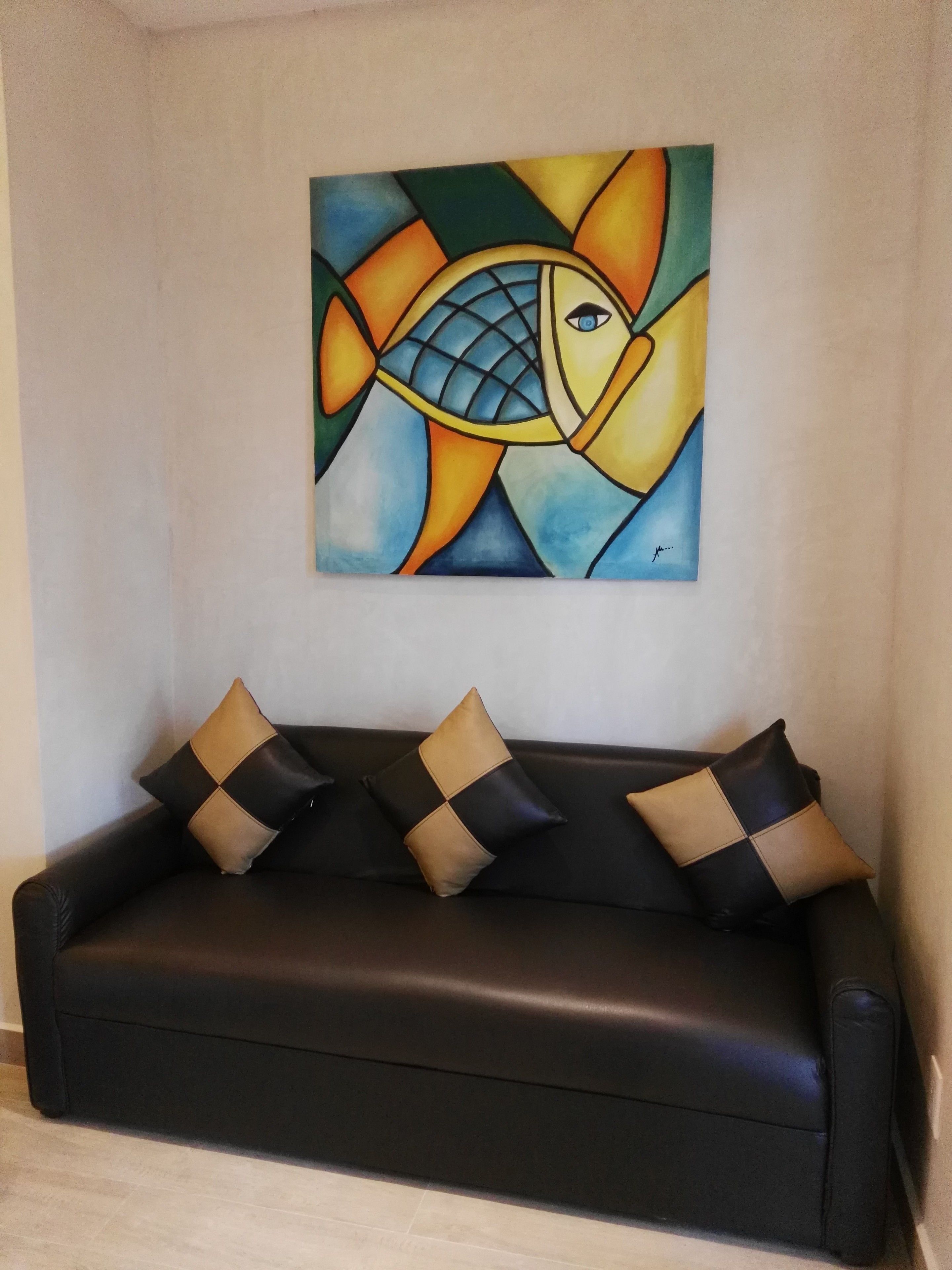 A black leather sofa with four cushions against a wall, above which is a colorful abstract painting.