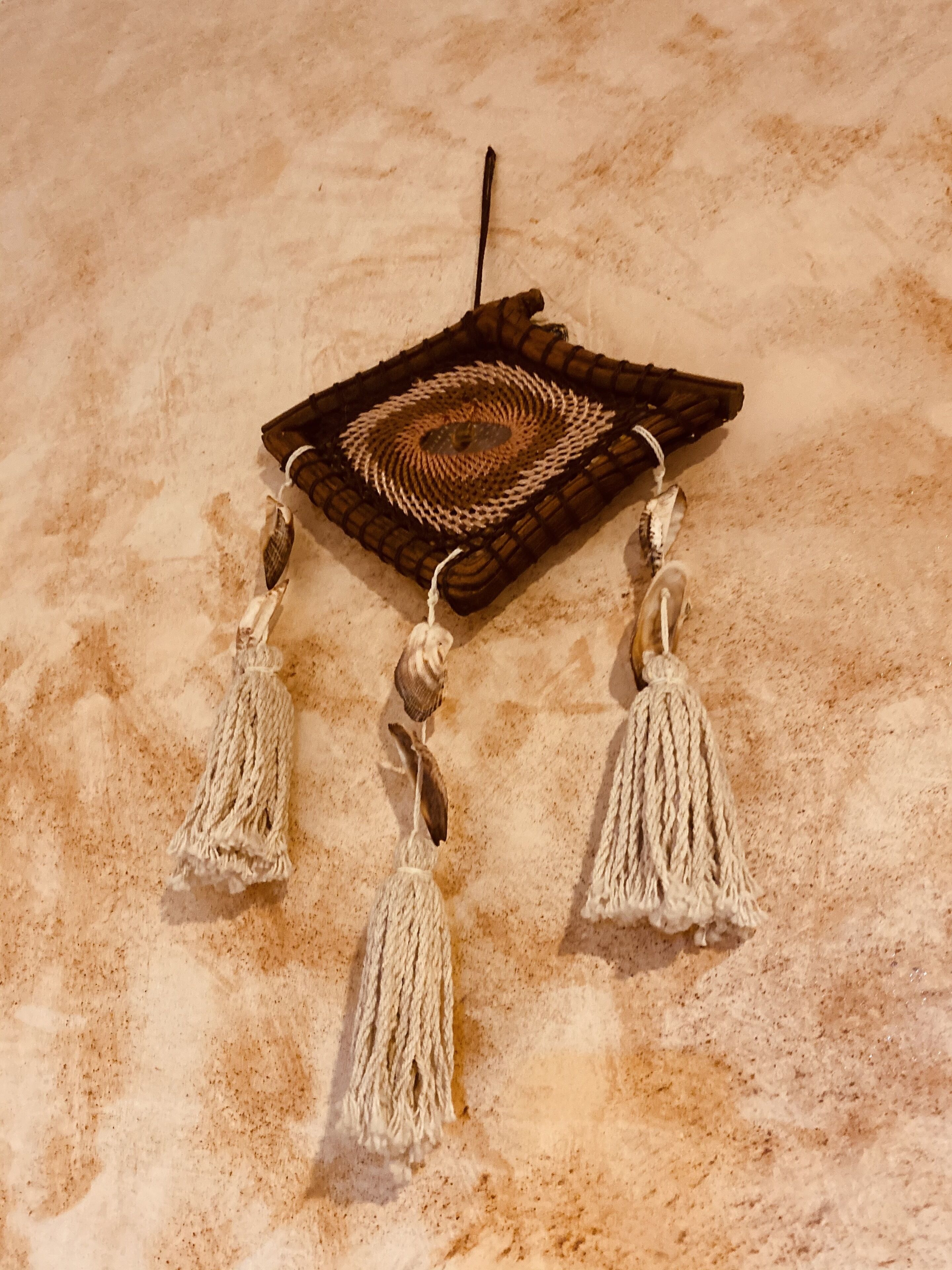 A woven dreamcatcher with tassels on a sandy surface.