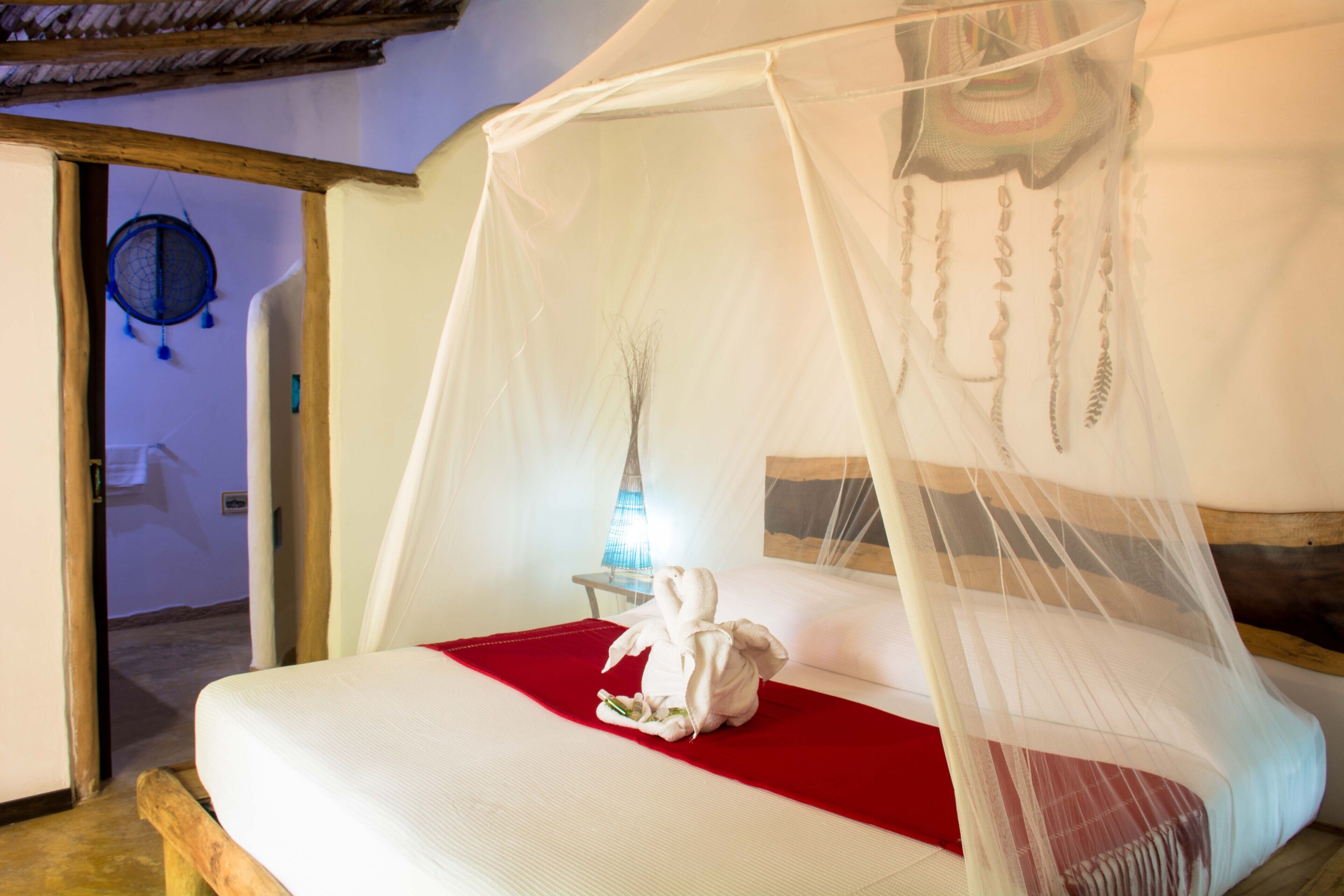 A bed with a white canopy, a red bedspread, and a towel on the bed.