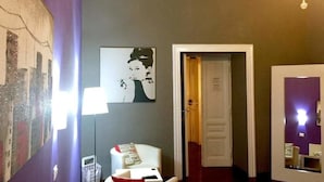 Un pasillo con una puerta, una pared con un cartel y una silla blanca con una revista.