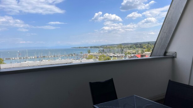 A balcony with a view of a marina, boats, and a distant shoreline. - Gästehaus Centro (Konstanz)