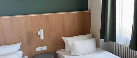 A hotel room with two beds, a small table, a wall-mounted light, and a framed picture of a sailboat.