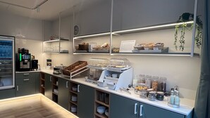 A modern breakfast bar with a coffee machine, shelves with glassware, and a clock on the wall. - Gästehaus Centro (Konstanz)