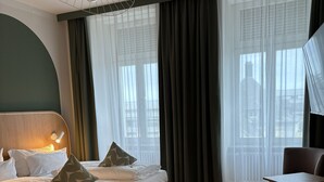 A modern hotel room with a bed, a desk, and a view of the city. - Gästehaus Centro (Konstanz)