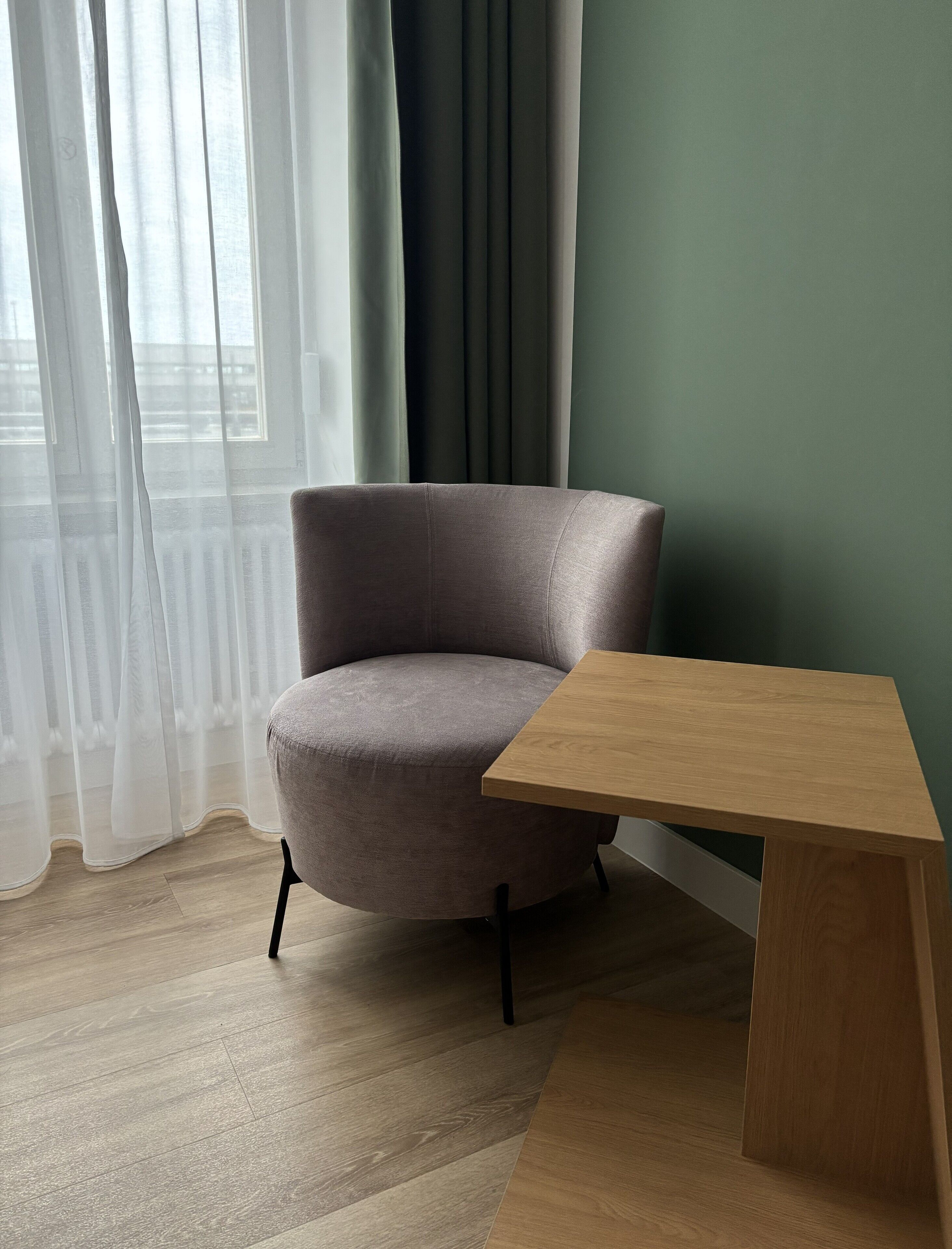 A room with a grey armchair, a wooden side table, and a green wall.