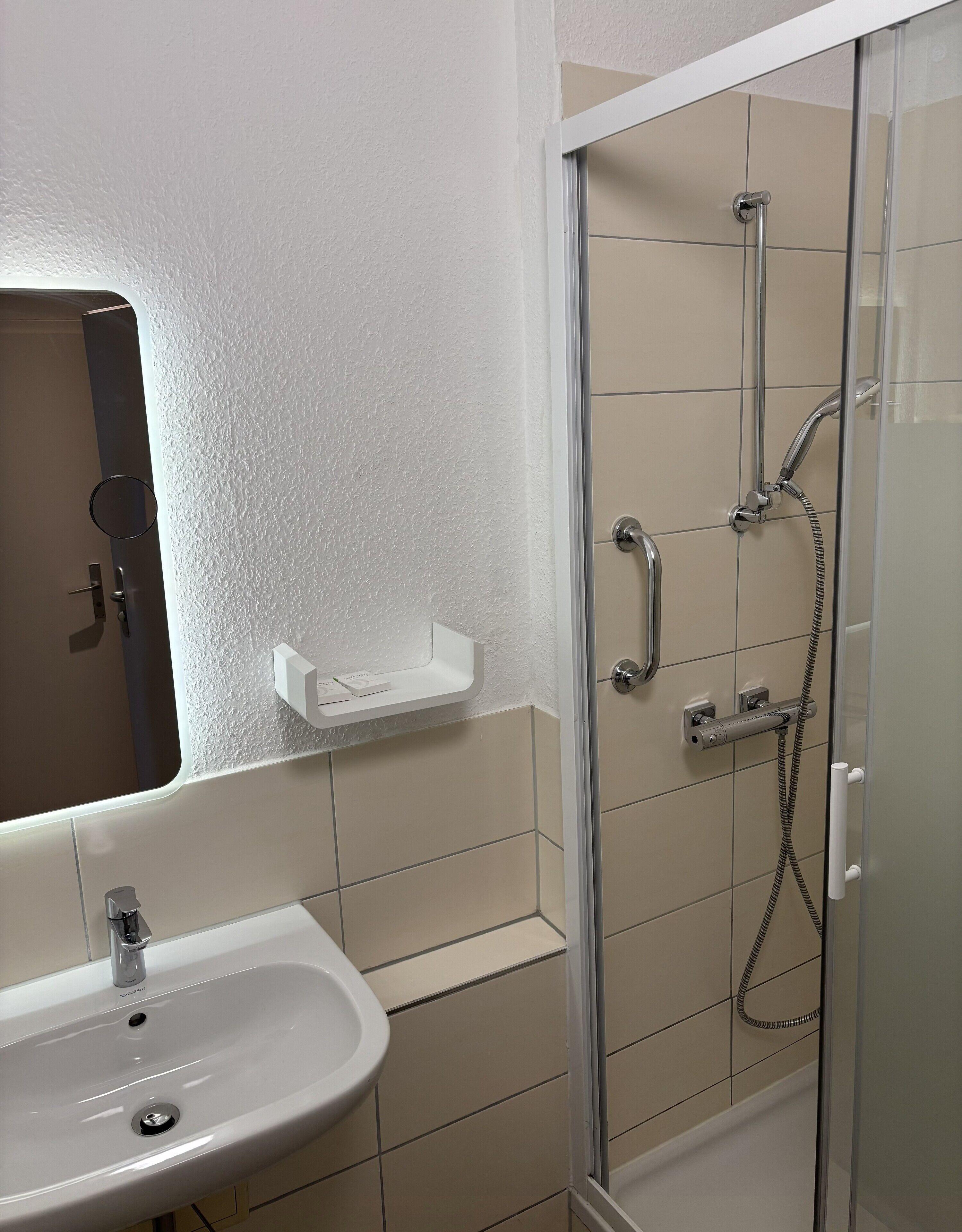 Un baño con un lavabo blanco, una ducha con mampara de vidrio y un espejo con marco blanco.