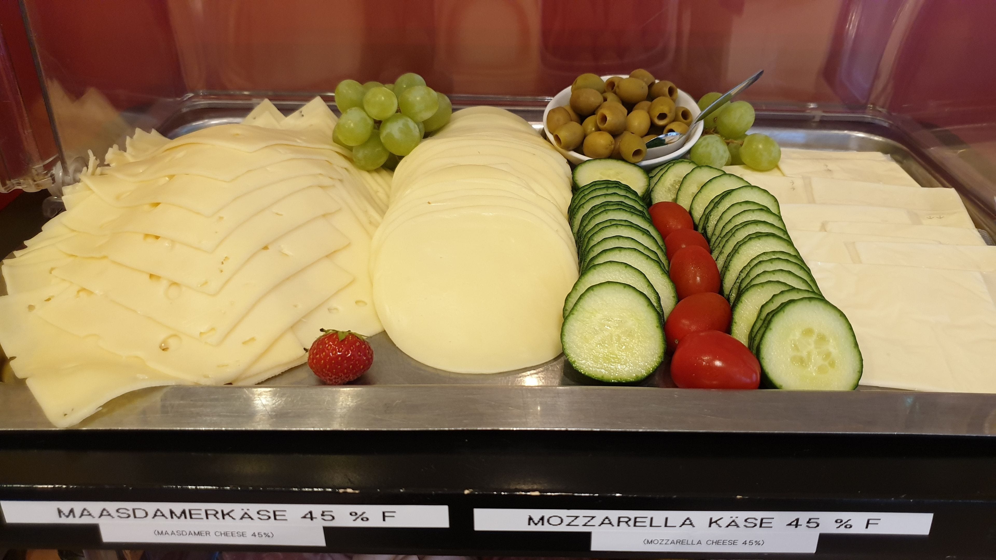 Exhibición de queso y fruta con etiquetas que indican 'Maasdamerkase 45% F' y 'Mozzarella Kase 45% F'.