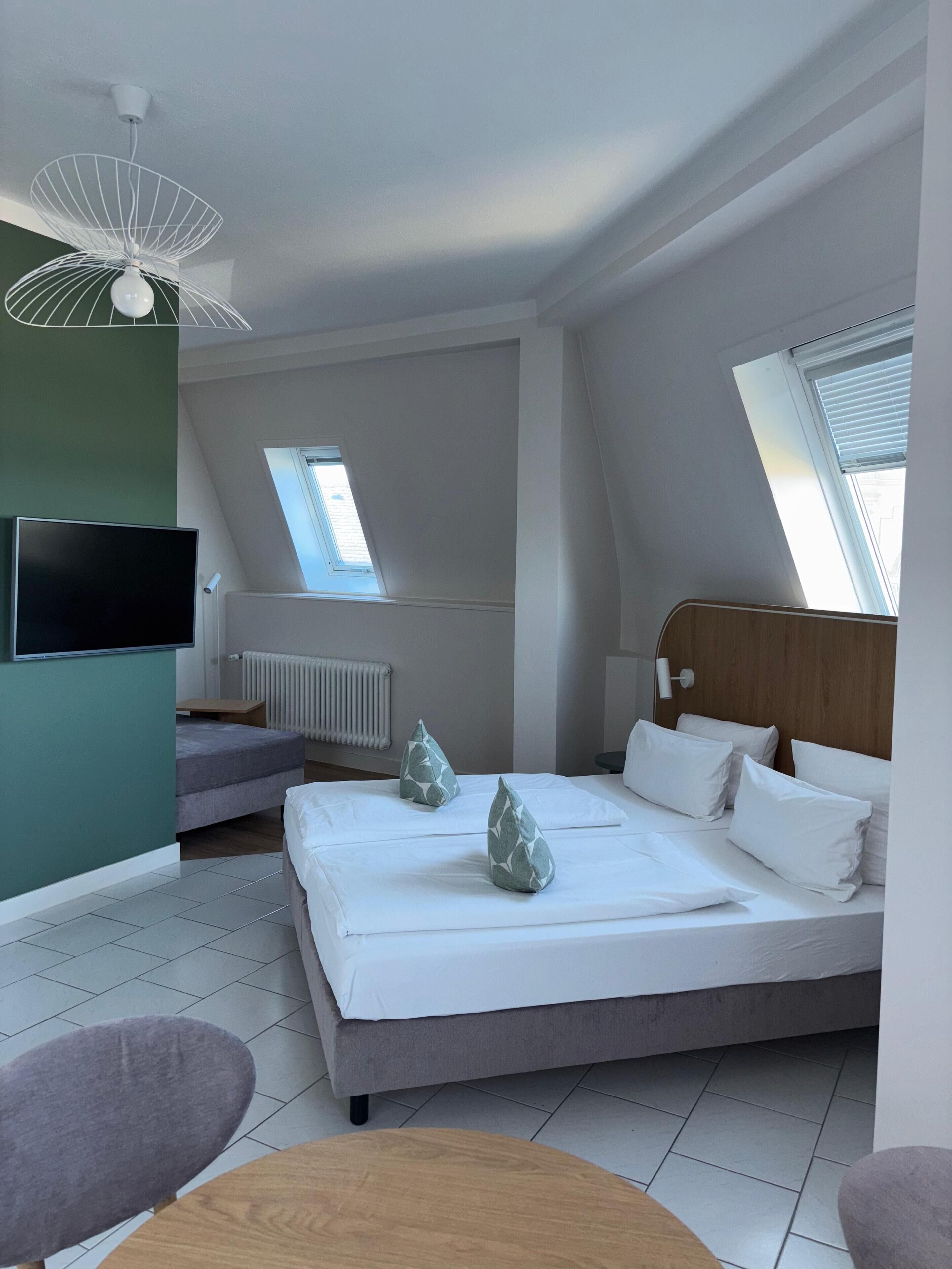 Ein modernes Schlafzimmer mit Bett, Schreibtisch, Stuhl, Fernseher und Deckenventilator.