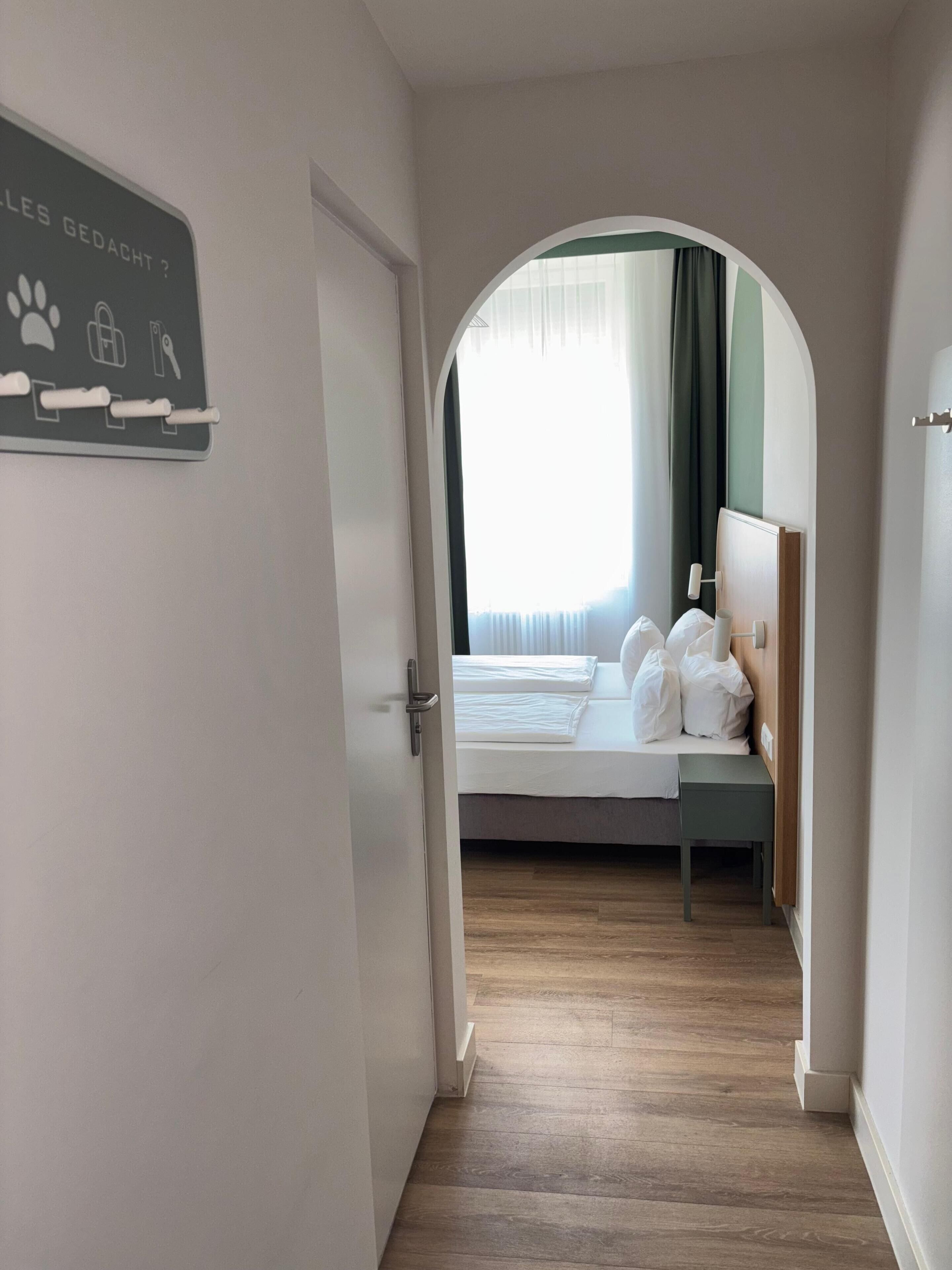 Habitación de hotel con cama, mesita de noche y ventana con cortinas.