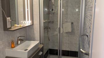 Un baño moderno con ducha envuelta en vidrio, tocador con lavabo y espejo con iluminación integrada.