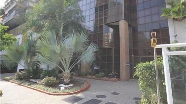 A modern building with a glass facade, surrounded by a landscaped garden with palm trees and shrubs. - GoHouse Torre do Barao 506 (Rio de Janeiro)