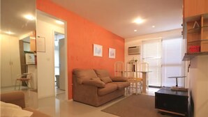A living room with a brown sofa, a coffee table, and a TV stand. There is a dining table with chairs in the background. - GoHouse Torre do Barao 506 (Rio de Janeiro)