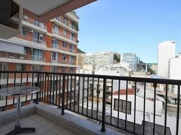 A balcony with a table and chairs, overlooking a cityscape with various buildings.