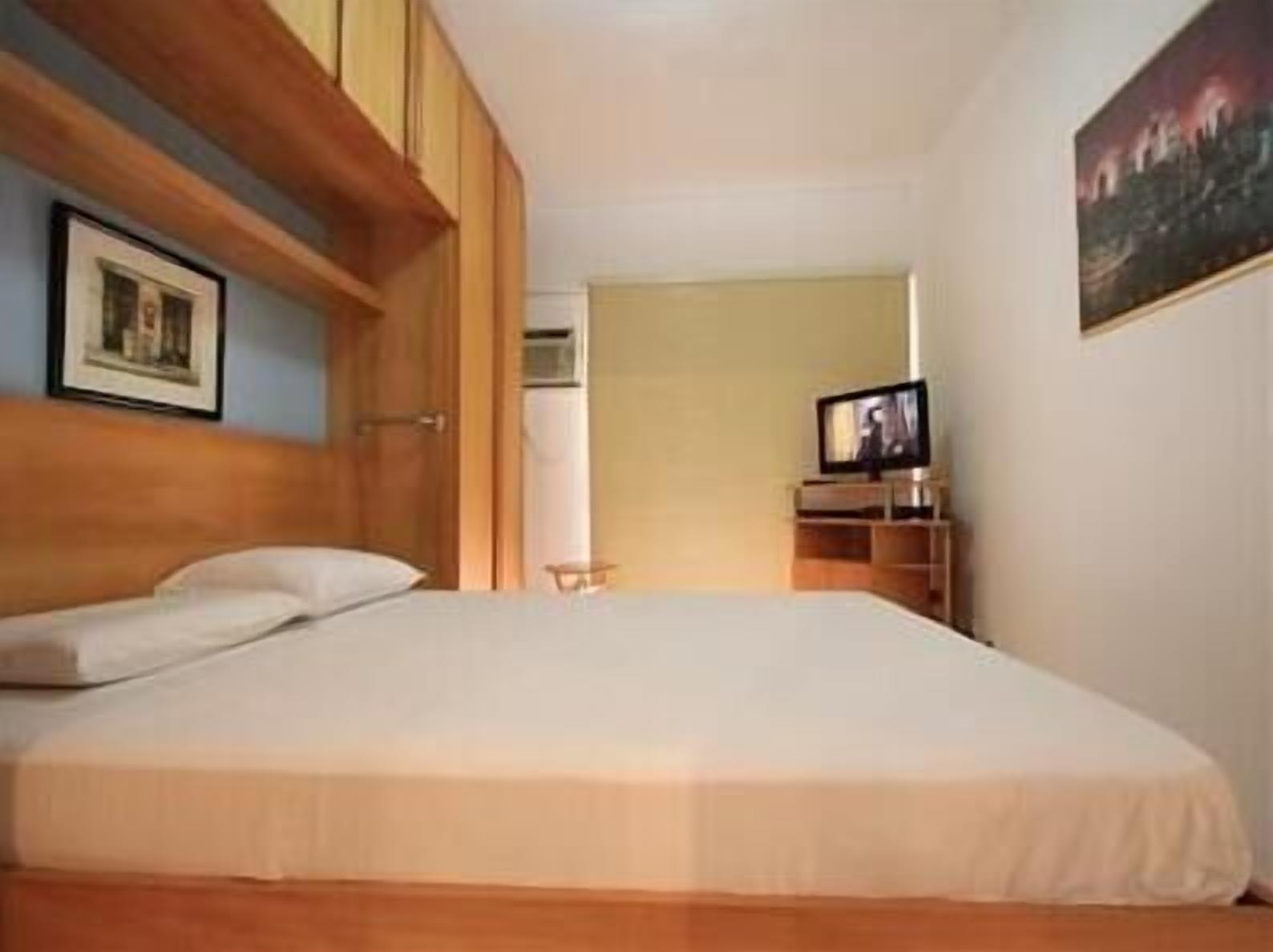 A bedroom with a bed, a television, and a painting on the wall.
